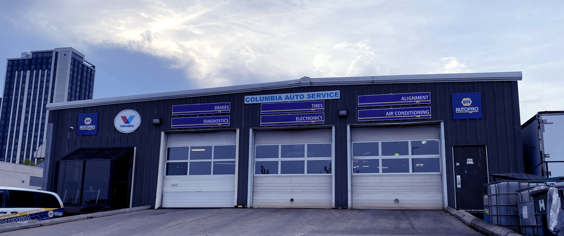 This image shows the exterior of "Columbia Auto Service," a vehicle repair shop offering services like brakes, alignment, and air conditioning, with a clear sky above.
